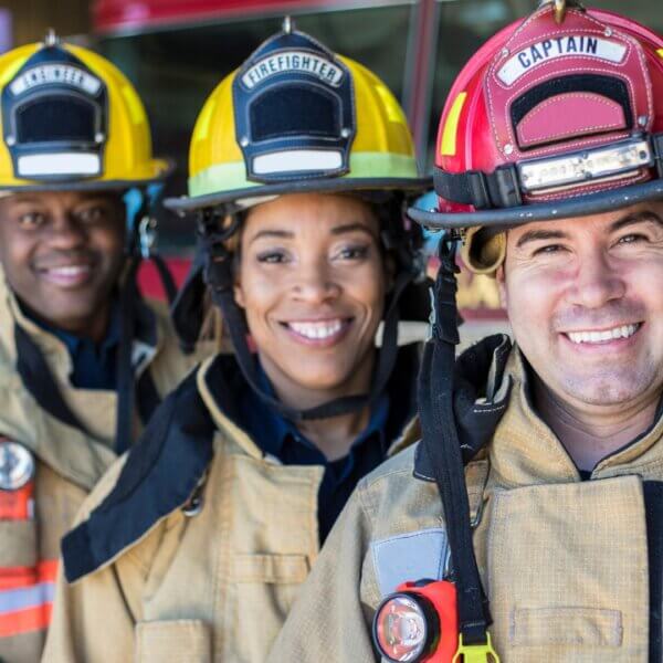 Three smiling firefighters wearing helmets and gear