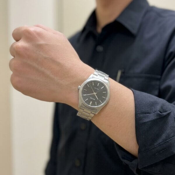 A detailed close-up highlights a functional silver wristwatch on a wrist against a uniform shirt.